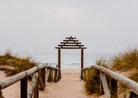 Wooden walkway through sand dunes leading to the tranquil shore in Cádiz, Spain.